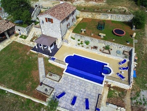 Eine Vogelperspektive auf ein Anwesen mit Swimmingpool, Liegestühlen und einem Steinhaus.