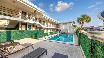 Een hotel met een zwembad, terras en een palmboom.