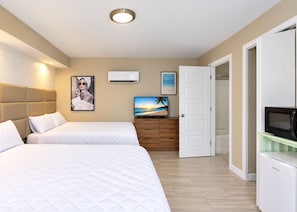 Ett hotellrum med två sängar, en tv, en luftkonditioneringsanläggning och en dörr som leder till ett annat rum.