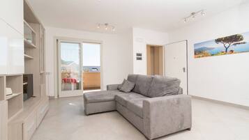 A modern living room with a grey sectional sofa, a built-in TV unit, and a sliding glass door leading to a balcony.