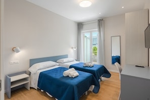 A hotel room with two beds, a desk, a chair, a TV, and a window with curtains. - Maison Le Sirene - Melodia (Massa Lubrense)