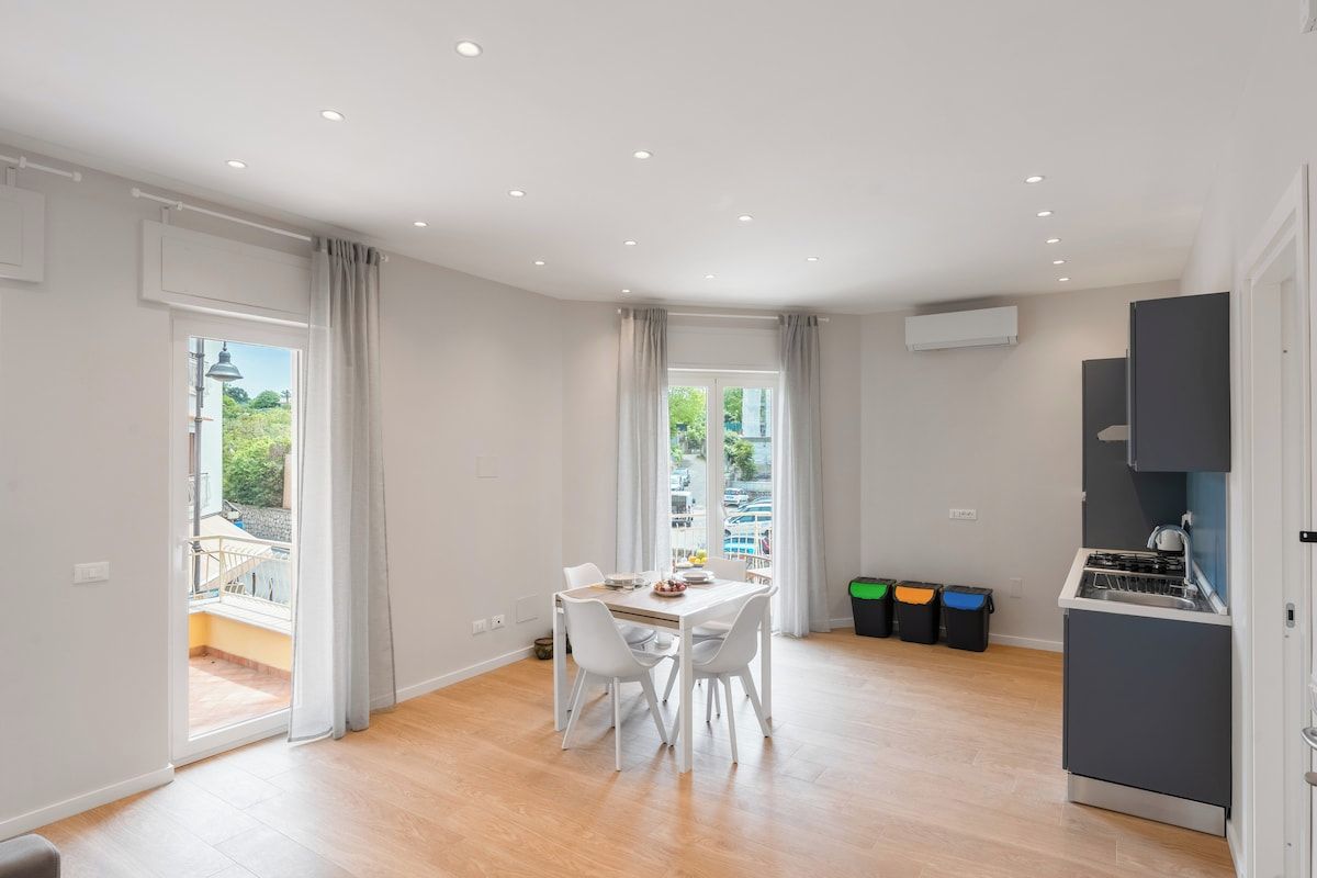 Eine moderne Küche mit Einbauherd, ein Essbereich mit Tisch und Stühlen und ein Blick ins Freie durch große Fenster.