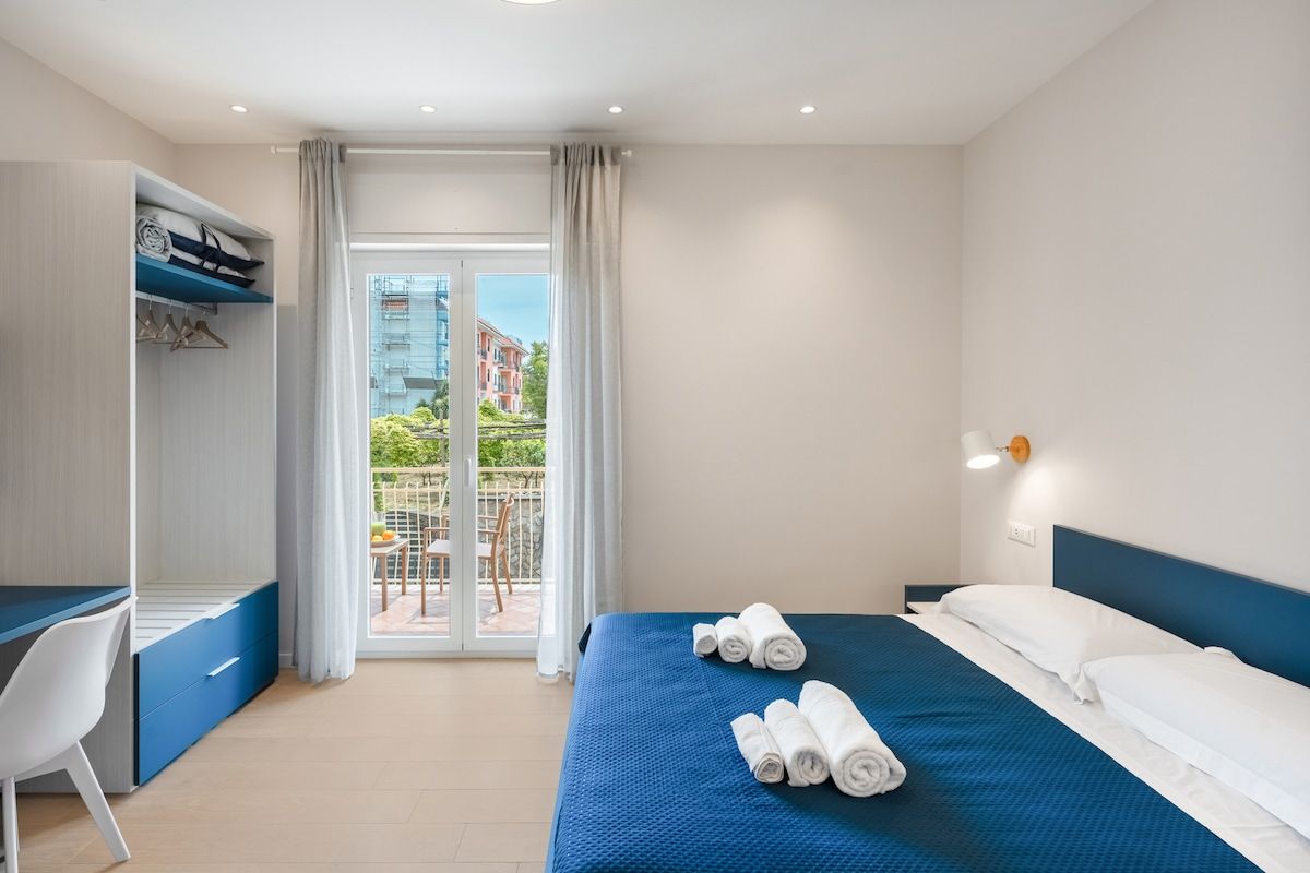 A hotel room with a bed, a desk, and a view of the outside.