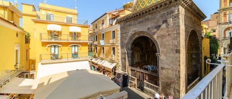 A square with a stone archway, yellow buildings, and outdoor seating.