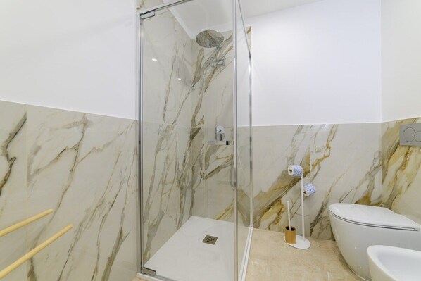 A bathroom with a glass-enclosed shower, a toilet, and marble walls. - Angela's room Sorrento (Sorrento)