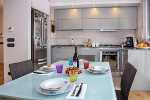 A modern kitchen with stainless steel appliances, a dining table set with plates, glasses, and cutlery, and a refrigerator adorned with magnets and photos. - Maya Penthouse - Sorrento Center (Sorrento)