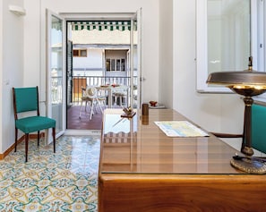 A room with a wooden desk, a green chair, a map on the desk, and a view of a balcony with outdoor furniture. - La Deliziosa - Sorrento (Sorrento)