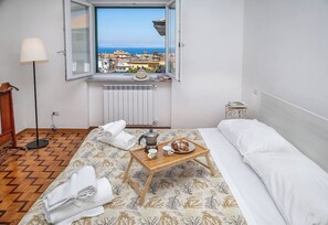A hotel room with a bed, a wooden bedside table with a tray of breakfast, a radiator, a floor lamp, and a window with a view of buildings and the sea. - La Deliziosa - Sorrento (Sorrento)