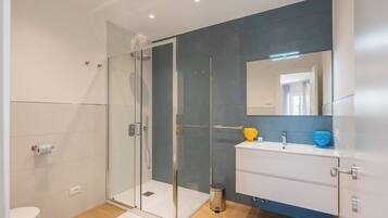 Ein modernes Badezimmer mit Duschkabine aus Glas, einem weißen Waschbecken und einem großen Spiegel.
