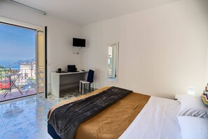 Quarto de hotel com cama, escrivaninha, cadeira, televisão e varanda com vista.
