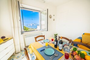 Ein Essbereich mit Tisch für zwei Personen, Blick aufs Meer und einem Fenster mit Vorhängen.