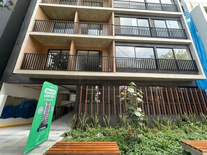 Ein mehrstöckiges Gebäude mit Balkonen, einem grünen Banner und einem Garten.