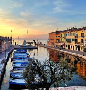 A canal with boats docked, buildings on the right, and a clear sky. - VILLA AUGUSTA: lake views and private lake access, fantastic pool (Lazise)