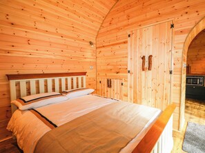 A wooden cabin room with a bed, a door, and a microwave in the corner. - Mallard Lodge (Marlow)