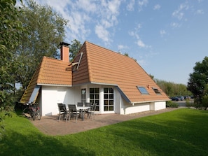 A house with a sloped roof, a chimney, and a patio with outdoor furniture. - Holiday Home in Dorum With Swimming Pool (Wurster Nordseeküste)