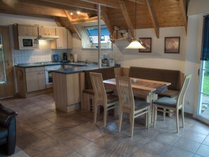 A kitchen with a central island, wooden cabinets, and a dining area with a bench and chairs. - Holiday Home in Dorum With Swimming Pool (Wurster Nordseeküste)