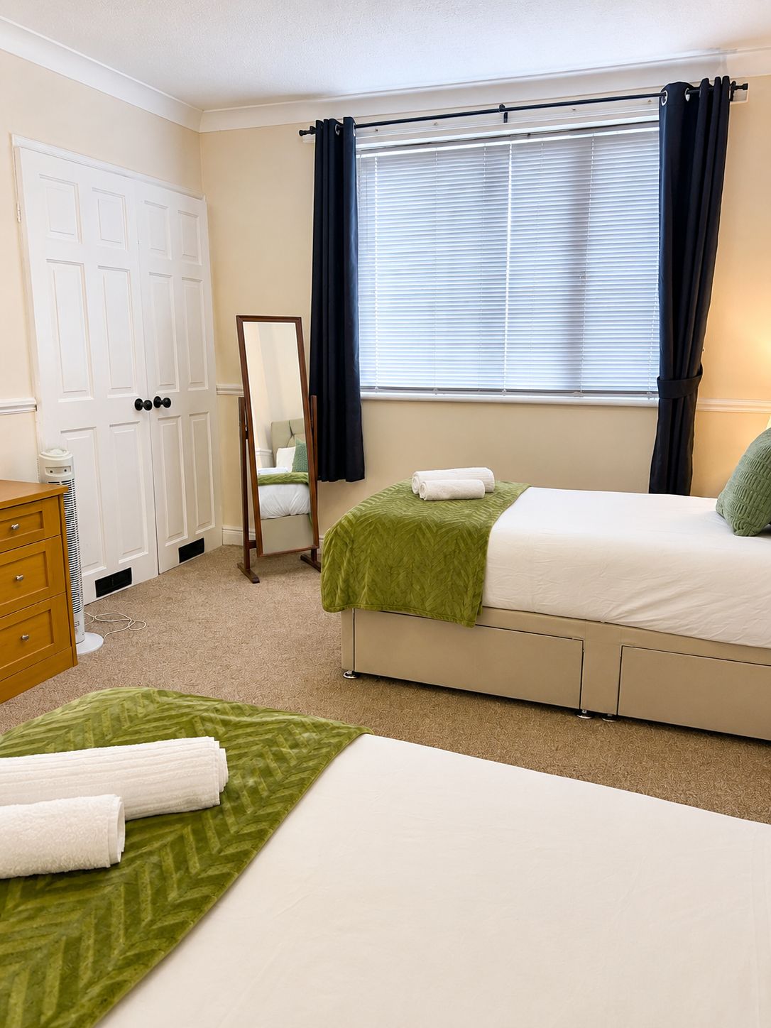 Une chambre à coucher avec un lit, une commode, un miroir et une fenêtre avec des rideaux.