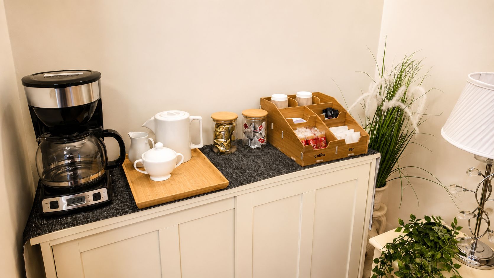 Eine Küchenarbeitsplatte mit Kaffeemaschine, einer weißen Tasse, einem Holzschneidebrett und einer Kaffeebar-Aufbewahrungsbox.