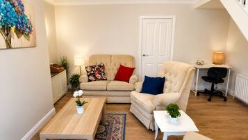 A living room with a sofa, armchair, coffee table, and a desk with a chair.