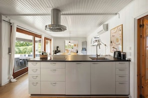 A modern kitchen with a central island, white cabinetry, and a stainless steel range hood. - Holiday home with large terrace in North Zealand (Vejby)