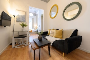 A modern living room with a black sofa, a glass coffee table, a TV mounted on the wall, and a large mirror. - M Cer822 Apartamento de 1 Dormitorio con Balc n (Madrid)