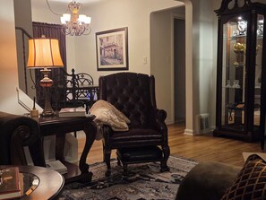 Ein Wohnzimmer mit einem dunkelbraunen Sessel, einem Tisch mit Lampe, einem gerahmten Bild an der Wand und einer Vitrine mit Dekoration.