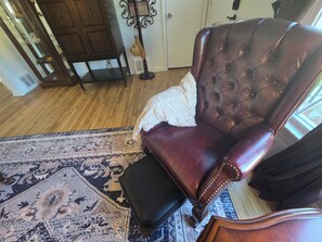 Una habitación con un sillón de cuero marrón oscuro, un cojín blanco, un tapete estampado y suelo de madera.