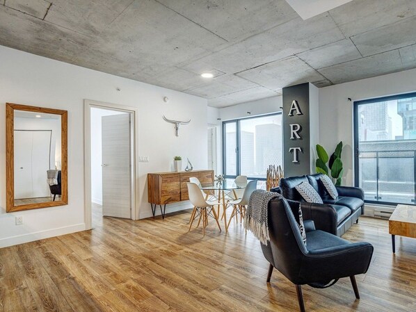 Un salon moderne comprenant un coin repas, un canapé en cuir noir, un meuble en bois et une grande fenêtre donnant sur la ville.