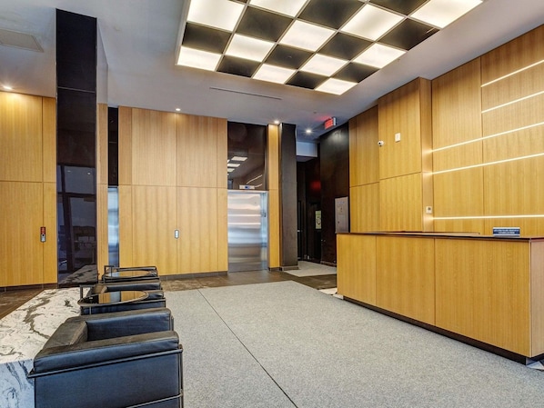 A modern lobby with a reception desk, seating area, and a staircase leading to an elevator. - Spacious 2 Bedroom Apartment with Modern Comforts | Le Smith (Montréal)