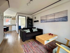 A modern living room with a sofa, a coffee table, and a rug. There is a kitchen area in the background. - Holiday Home With 3 Bedrooms (Oostkapelle)