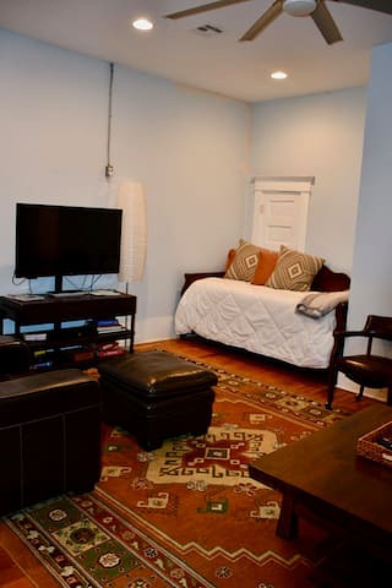 A room with a bed, a television, a ceiling fan, and a patterned rug.