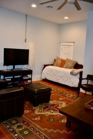 A room with a bed, a television, a ceiling fan, and a patterned rug. - Hideaway @ the Hill- A Downtown Pawhuska Loft (Pawhuska)