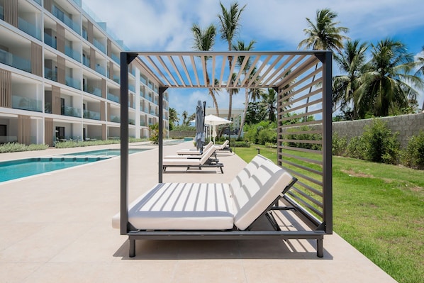 A modern outdoor pool area with lounge chairs and a pergola structure. - Born | Modern 2-bedroom apartment (Bávaro)