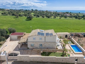 A stone house with a tiled roof, a swimming pool, and a view of a green field and coastline. - Holiday Home With 1 Bedroom (Ragusa)