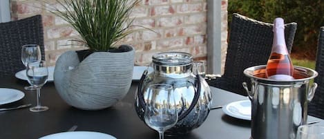 Mesa posta para refeição, com planta em vaso, jarra de metal e garrafa de champanhe.