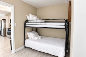 A bunk bed with white bedding in a room with beige walls and a wooden floor. - Tenth Avenue Beach Escape | Unit 229 (Myrtle Beach)