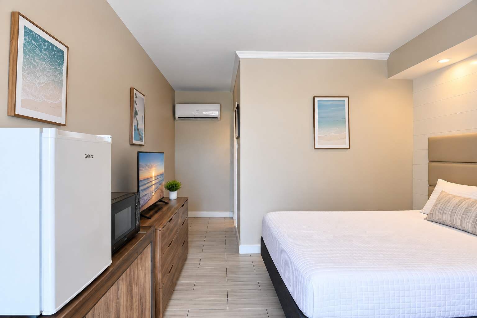 Een hotelkamer met een bed, een televisie, een koelkast en een wandairconditioner.