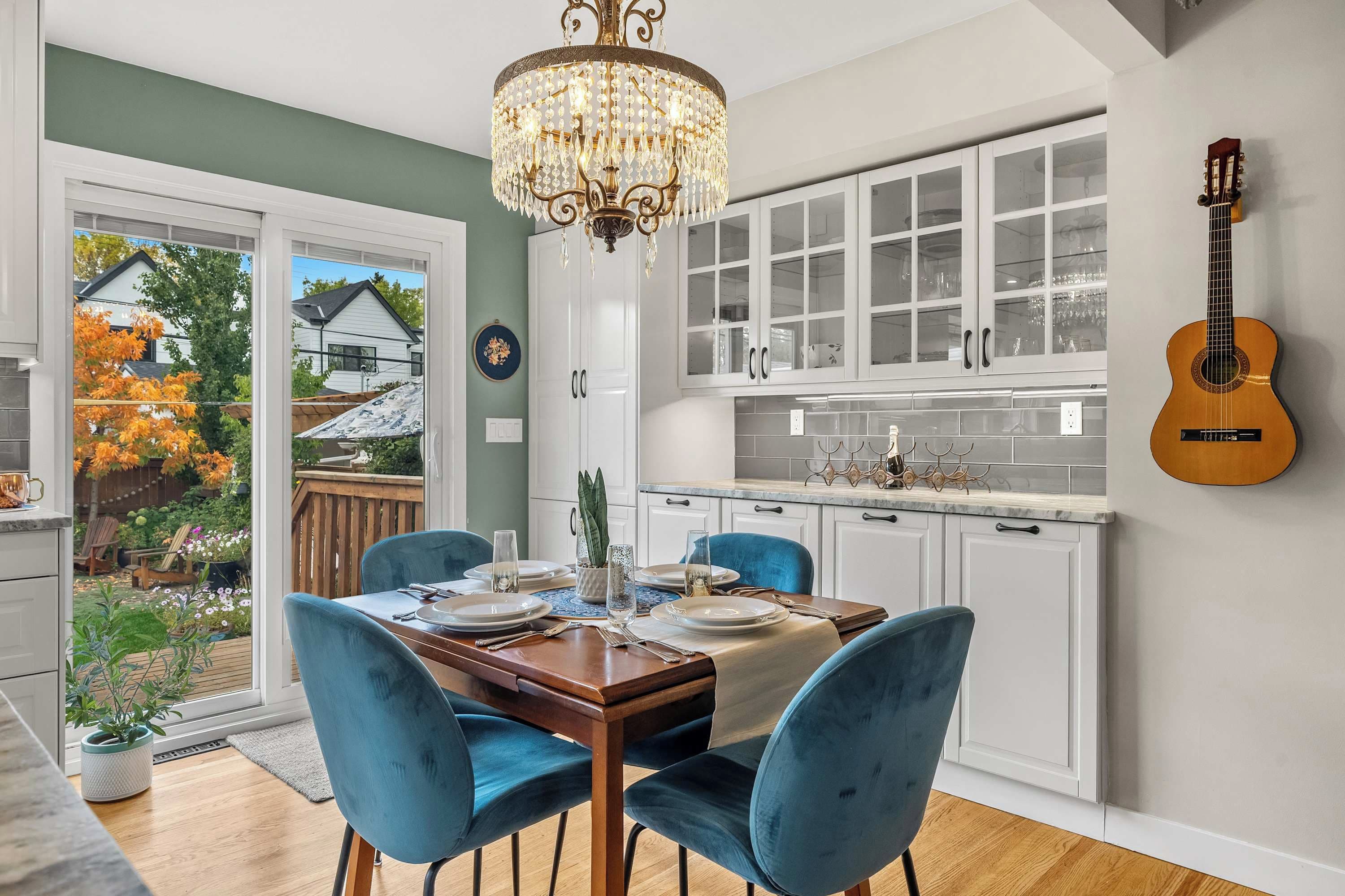 A dining area with a chandelier, a guitar, and a view of a house through a glass door.