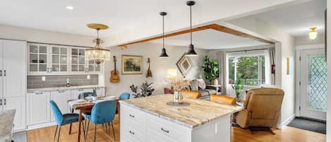 A spacious kitchen with white cabinets, a dining area with blue chairs, and a large island with drawers.