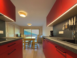 A modern kitchen with red cabinetry, a dining area with wooden chairs, and a view of a mountain landscape through a large window. - Roche Parstire 202 – Mountain view, resort centre, near the slopes (Beaufort)