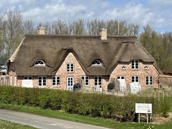 A traditional building with a thatched roof, multiple chimneys, and a sign in front. - "reethus" in the House on the Dike (Vollerwiek)