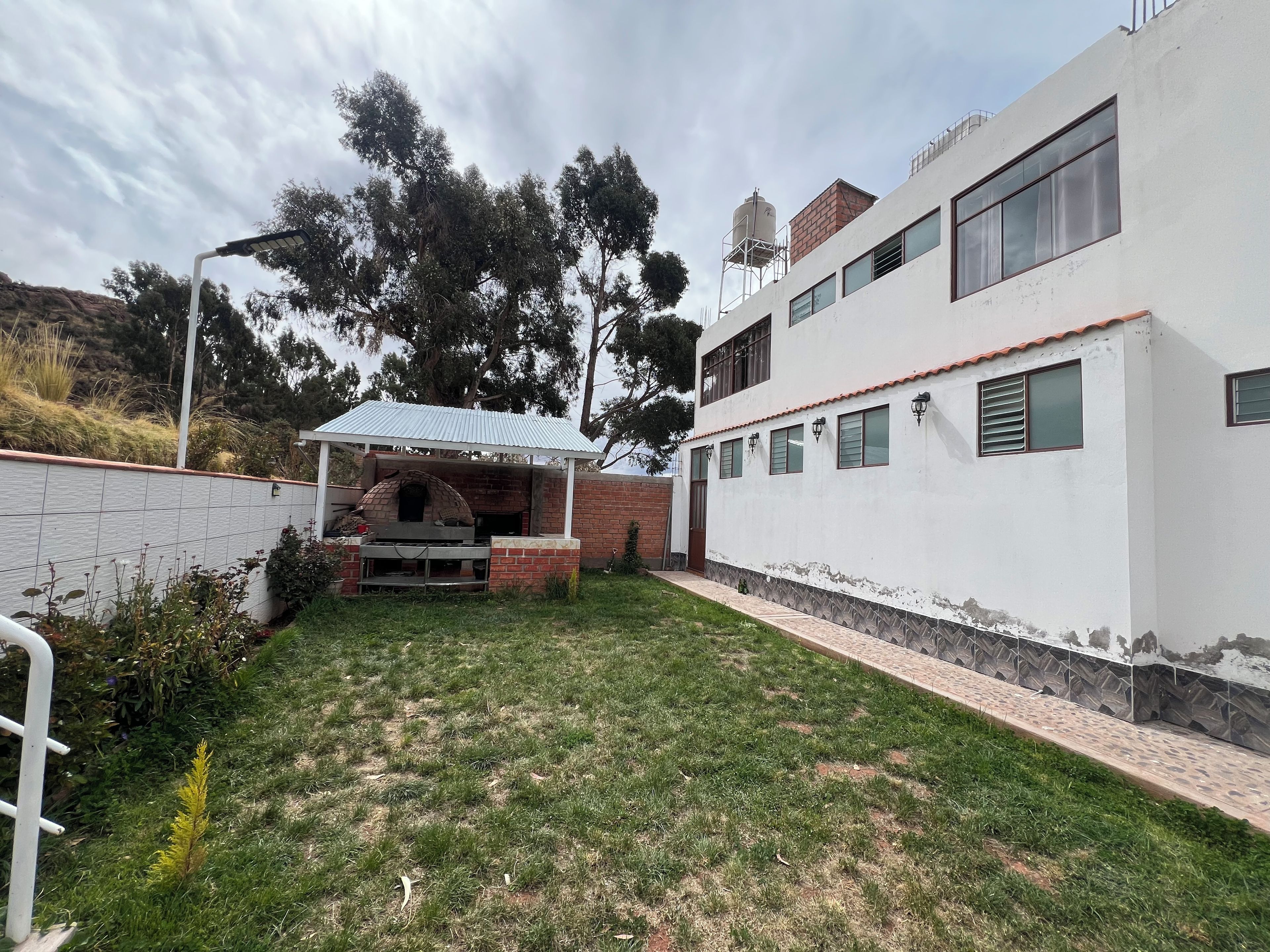 Una propiedad residencial con zona de barbacoa de ladrillo, un patio cubierto y un edificio blanco con varias ventanas.