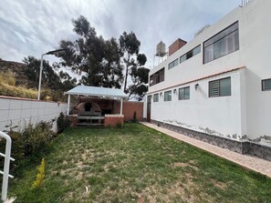Una propietat residencial amb zona de barbacoa de maó, terrassa coberta i edifici blanc amb nombroses finestres.