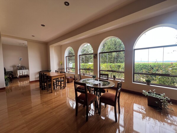 A spacious room with a dining area, large arched windows, and a view of greenery.