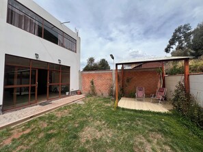 Edifici modern de dues plantes amb porta d'entrada de vidre, zona de terrassa coberta i dos seients de relaxació, i mur de maó.