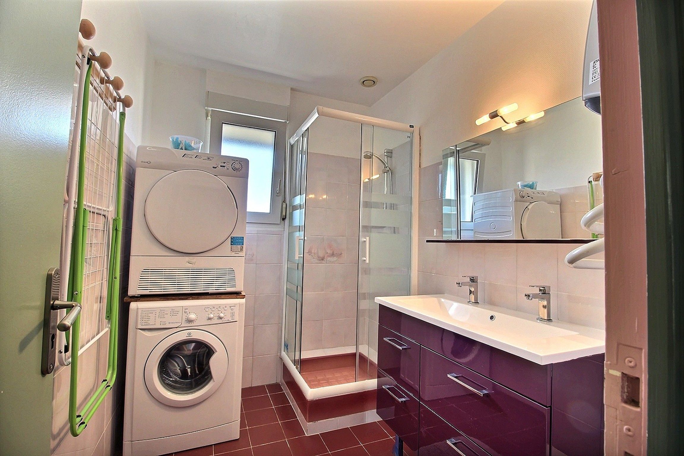 Une petite salle de bain équipée d’un lave-linge, d’une douche à parois de verre et d’un meuble-lavabo avec un miroir.