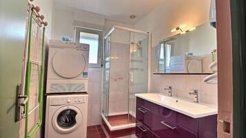 Une petite salle de bain équipée d’un lave-linge, d’une douche à parois de verre et d’un meuble-lavabo avec un miroir.