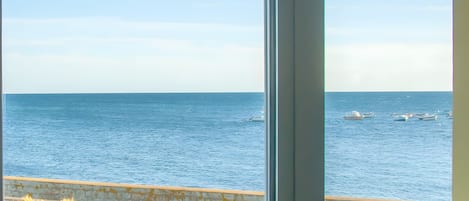 A view of the sea from a window, with a wooden railing and a yellow container on the windowsill.