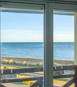 A view of the sea from a window, with a wooden railing and a yellow container on the windowsill.