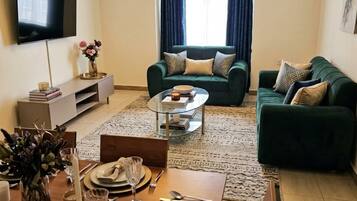 A modern living room with a dining area, a sofa set, a chandelier, and a flat-screen TV.
